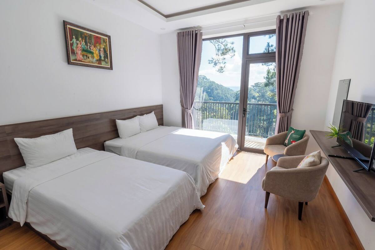 A hotel room with two beds, a balcony with curtains, a TV, and a painting on the wall.