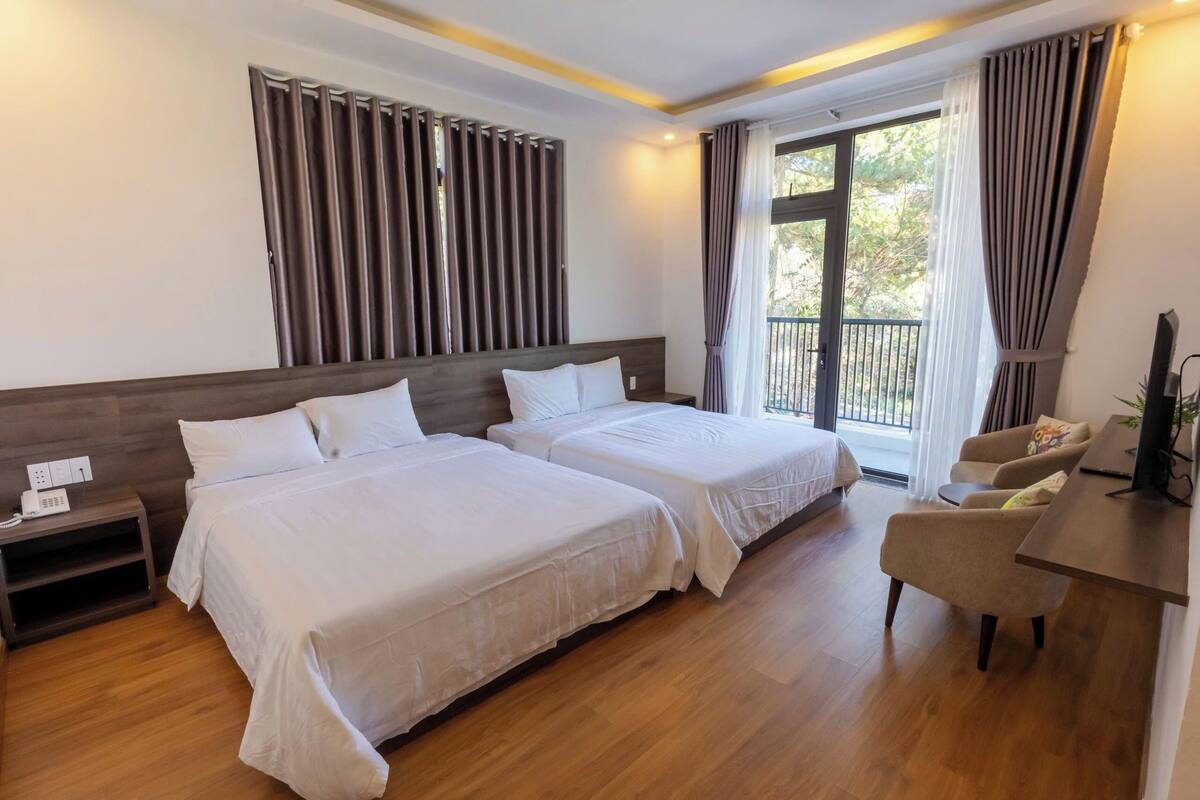 A hotel room with two beds, a desk, a chair, and a balcony with curtains.
