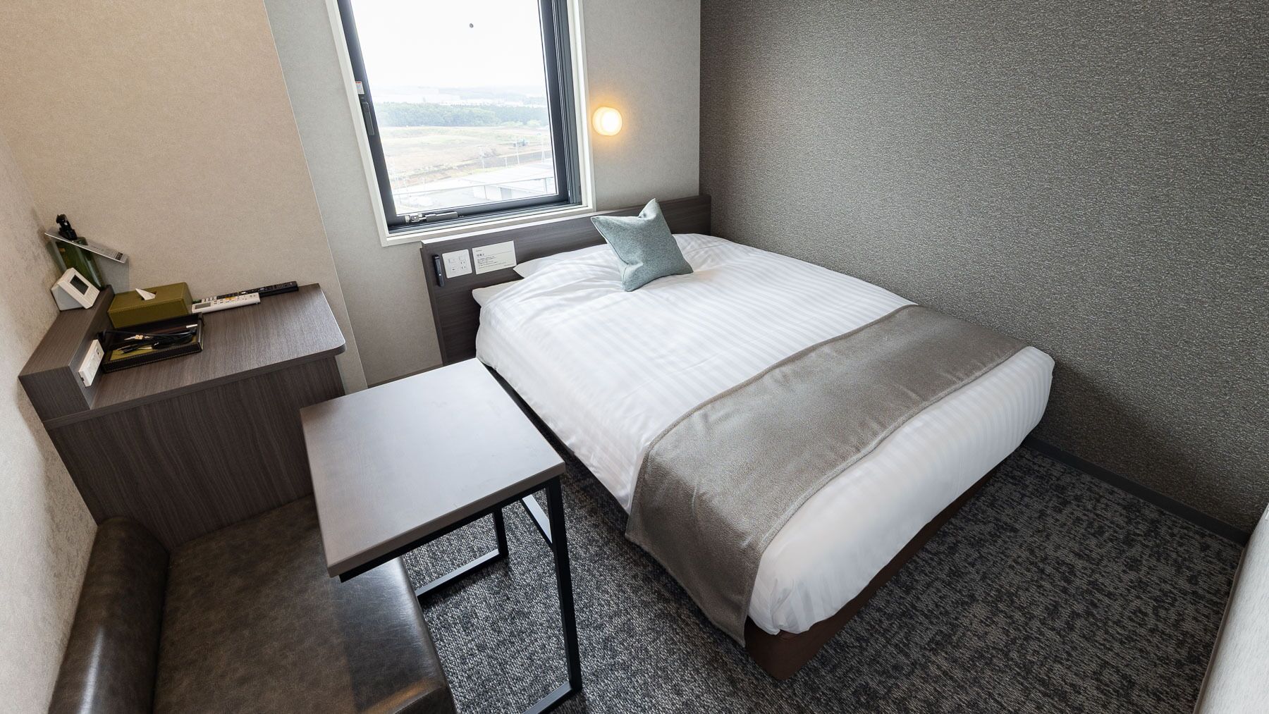 Une chambre d’hôtel de taille réduite, comprenant un lit, une table de chevet et un petit bureau.