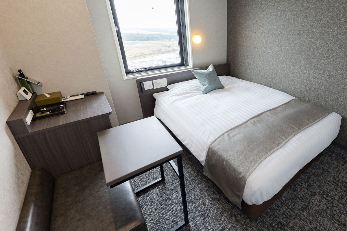 Ein gemütliches Hotelzimmer mit Bett, Nachttisch und einem kleinen Schreibtisch.