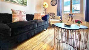 Ein modernes Wohnzimmer mit einem schwarzen Sofa, gemusterten Kissen, einer Stehlampe, einem runden Couchtisch und einem großen Fenster mit Vorhängen.