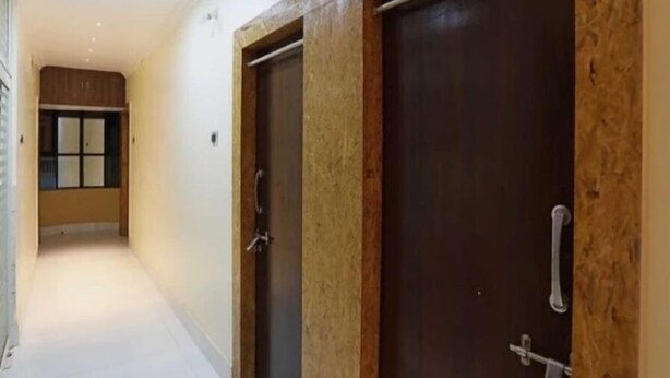 Un couloir avec deux portes en bois foncé, une fenêtre avec des stores et un plancher de couleur claire.