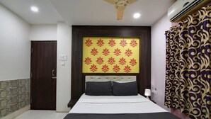 Une chambre d’hôtel avec un lit, un ventilateur de plafond, un appareil de climatisation, un rideau à motifs et une porte.