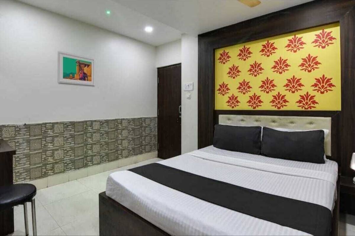A hotel room with a large bed, a headboard with a floral pattern, a small painting on the wall, and a patterned wall design.