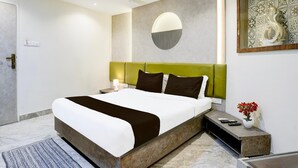 Une chambre d’hôtel moderne avec un grand lit, une tête de lit verte, un élément de décoration circulaire au mur, une petite table sur laquelle est posé un vase de fleurs et un ventilateur de plafond.
