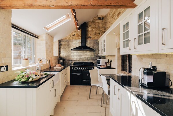 Une cuisine avec des meubles blancs, une cuisinière noire et un mur recouvert de pierres apparentes.