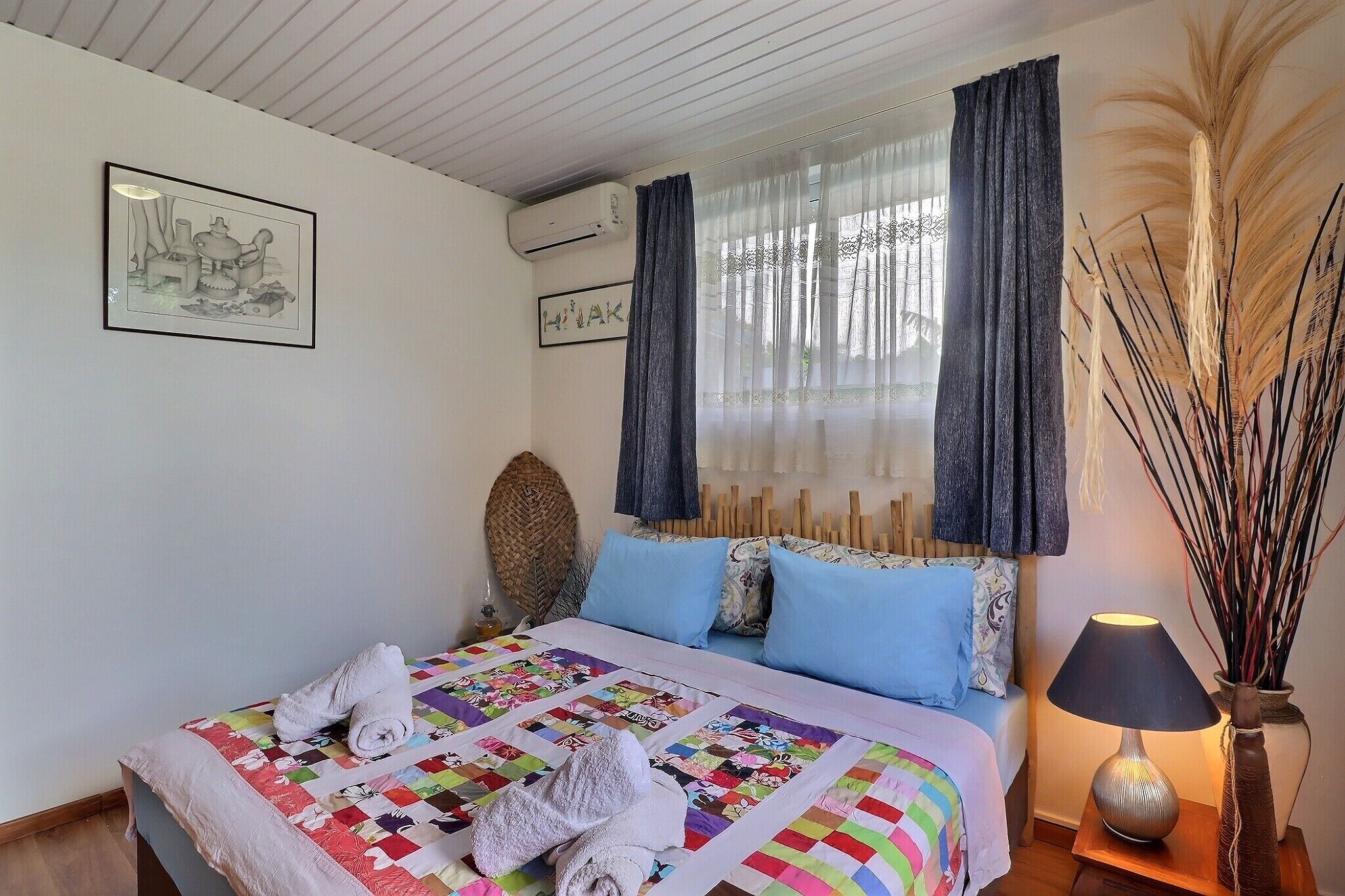 Una cama bien hecha con un edredón colorido, una lámpara de noche y una planta decorativa.