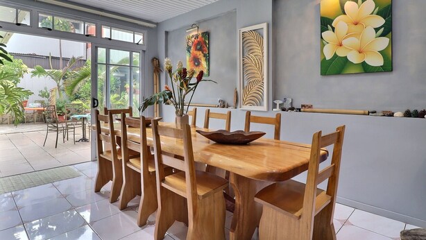 A dining area with a wooden table and chairs, a vase with flowers, and wall art. - Fare Nãhina - 2 chambres - Centre-Ville (Papeete)