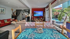 Un salon avec un téléviseur, un canapé rouge et un coin repas avec une table.