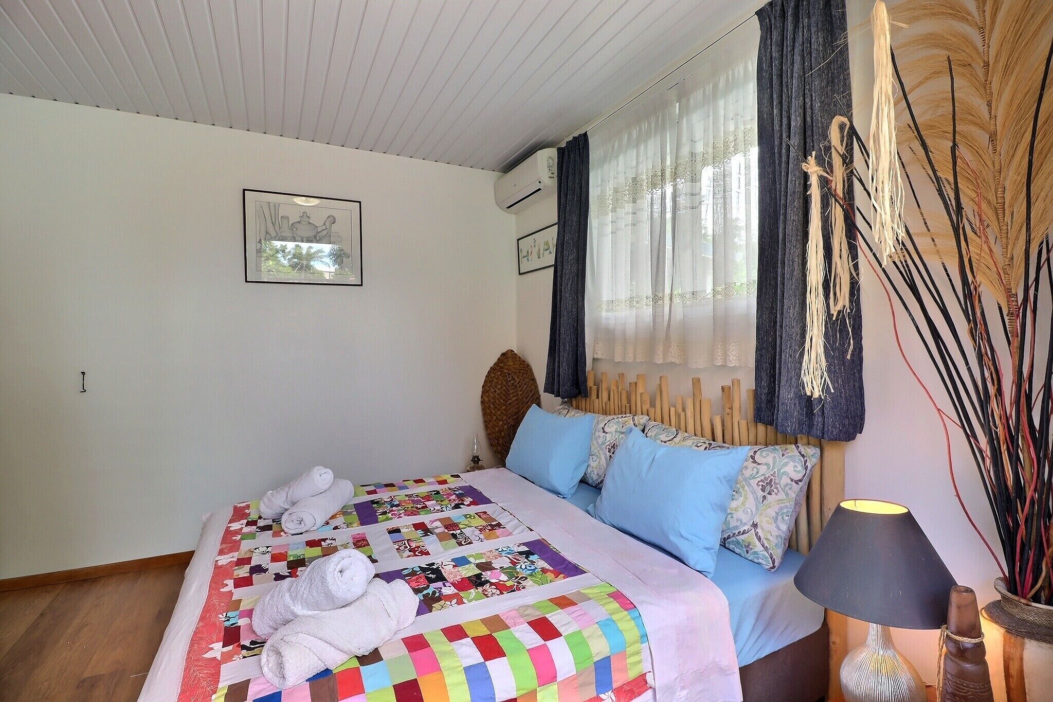 Ein Schlafzimmer mit Bett, Kissen, einer Nachttischlampe und einem Fenster mit Vorhängen.