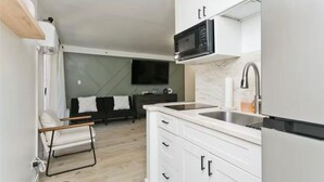 A modern kitchen with white cabinets, a stainless steel sink, and a black microwave. - Aloha Suite Near the Sea IV, 3 Block Walk to Beach (Honolulu)