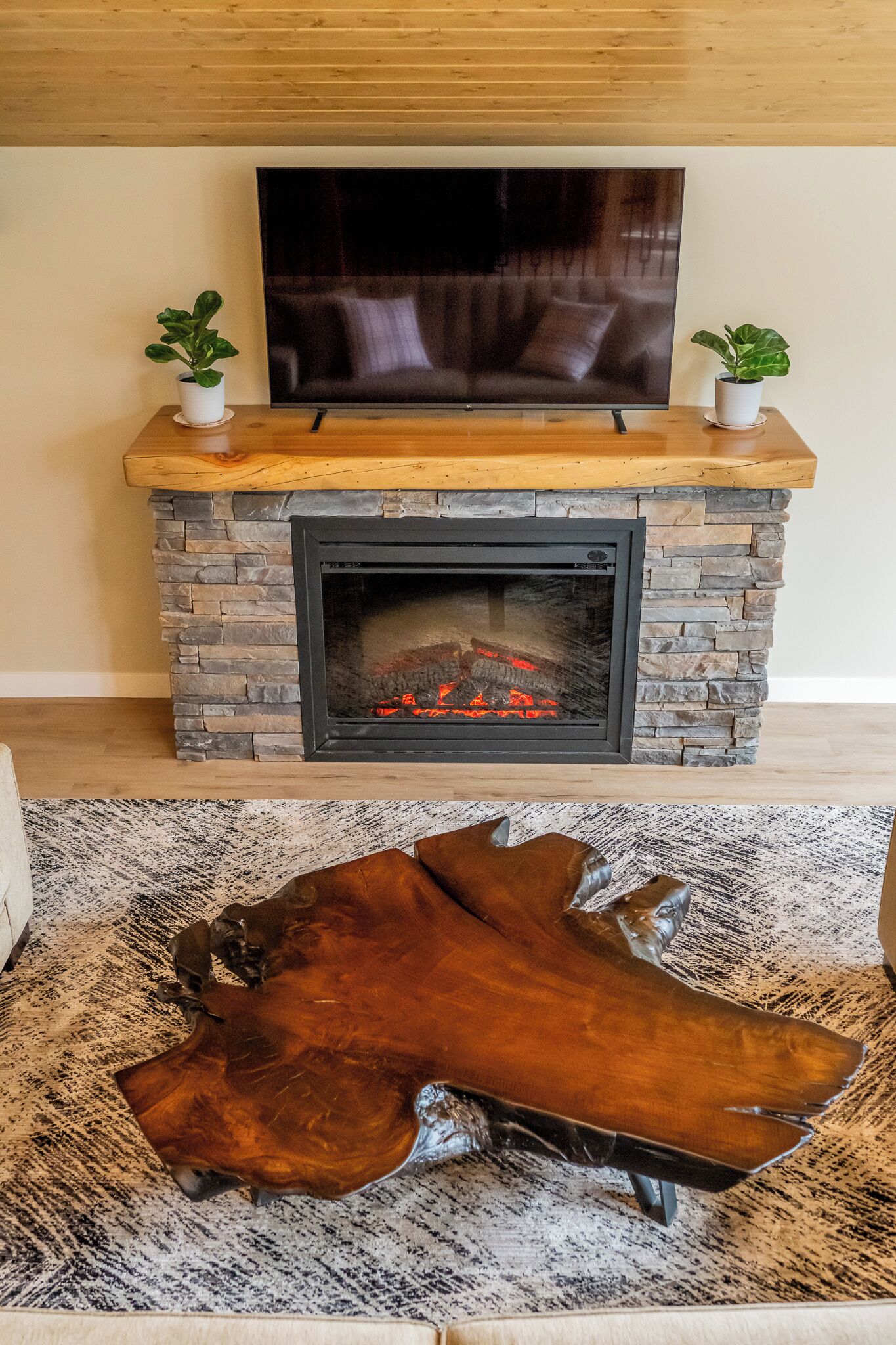 Una chimenea con revestimiento de piedra, un televisor de pantalla plana encima y una mesa de centro de cuero al frente.