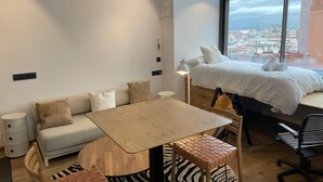 A modern room with a bed, a sofa, a small table, a desk, and a chair. There is a window with a city view. - Modern Loft with Panoramic Views (Madrid)