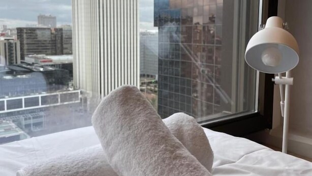 A bed with white bedding and a view of a cityscape through a window. - Modern Loft with Panoramic Views (Madrid)