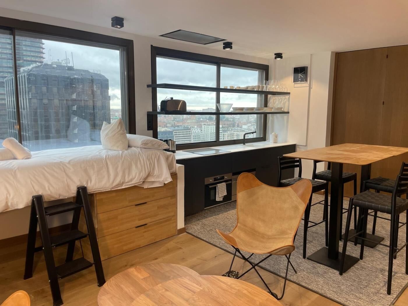 Ein modernes Hotelzimmer mit Bett, Schreibtisch, Esstisch und Blick auf die Stadt.