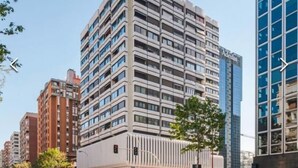 A modern high-rise building with a unique architectural design, featuring multiple balconies and a prominent entrance with a curved facade. - Chic Studio Loft with City Views (Madrid)