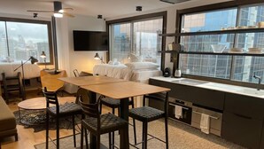 A modern hotel room with a dining area, a bed, a TV, and a large window with a city view. - Chic Studio Loft with City Views (Madrid)