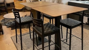 A modern hotel room with a wooden dining table, black upholstered chairs, a bed with white linens, a flat-screen TV mounted on the wall, and a window with a city view. - Chic Studio Loft with City Views (Madrid)