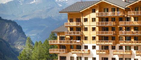A multi-story wooden building with balconies, set against a mountainous backdrop.
