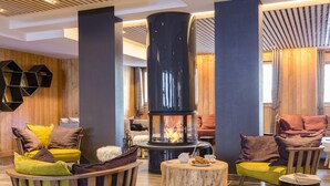 Hyggelig lounge med en centralt placeret brændeovn, behagelige siddepladser og en trævæg.