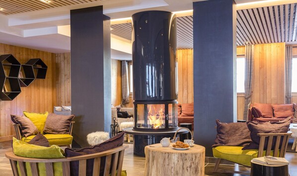 Un espace salon chaleureux avec un poêle à bois central, des sièges confortables et un mur en bois.