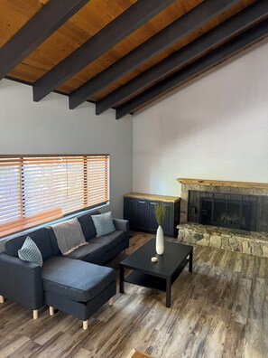 A modern living room with a sectional sofa, a fireplace, and a wooden ceiling.