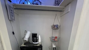 Una kitchenette compacta con refrigerador, cafetera y un pequeño basurero.