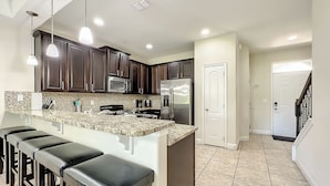 A modern kitchen with dark wood cabinets, stainless steel appliances, a granite countertop, and a bar area with stools.