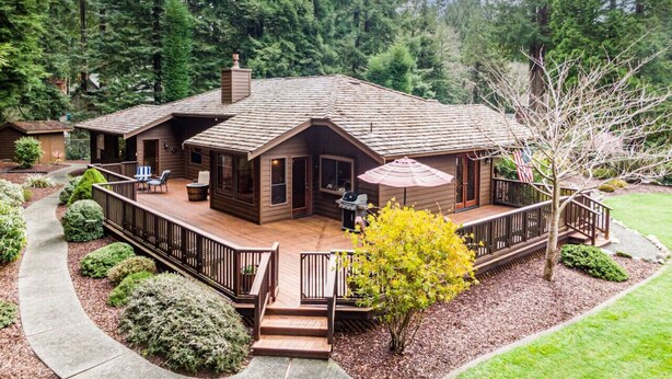 A cabin with a deck, surrounded by trees and a garden path.