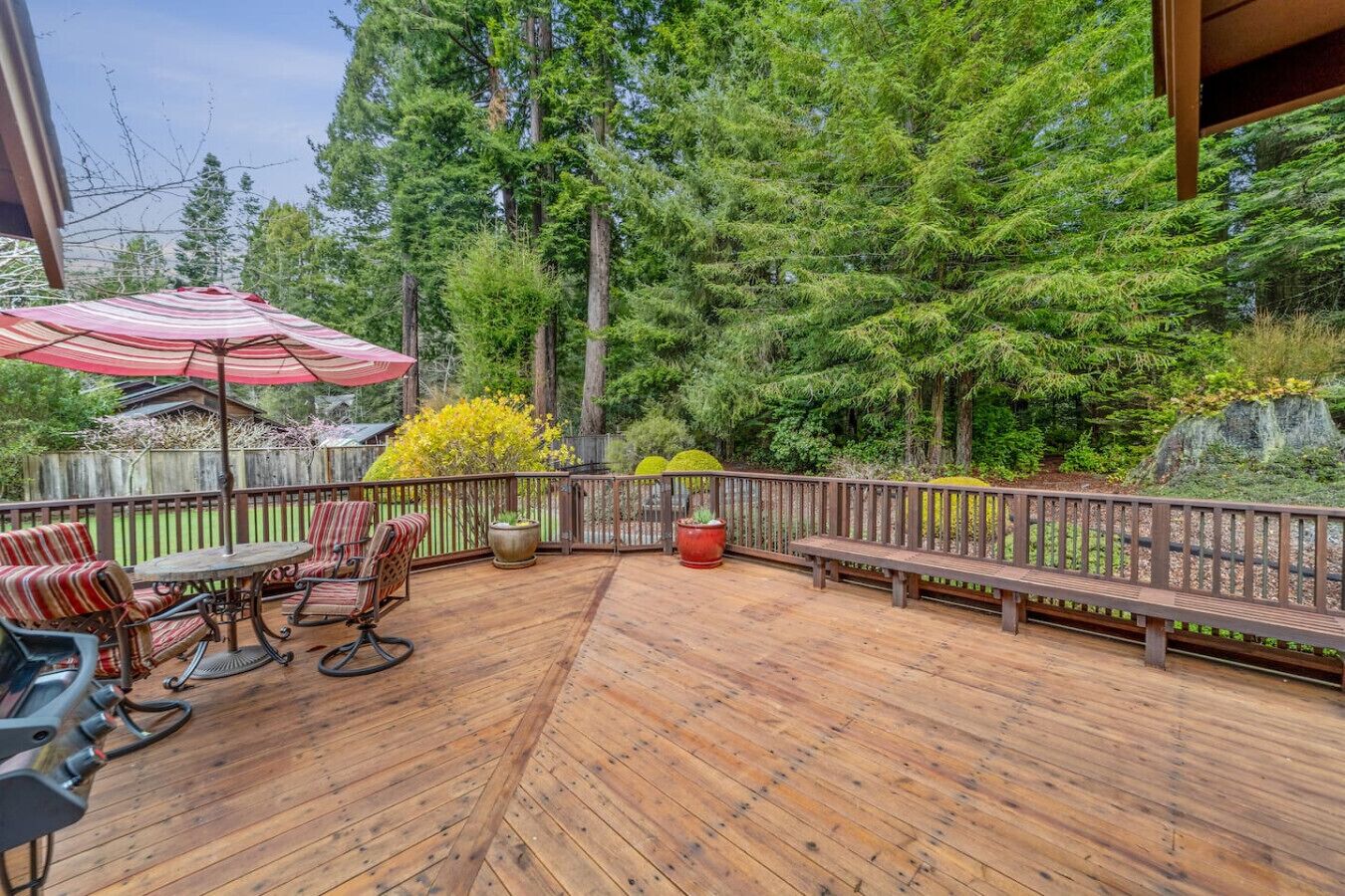 A wooden deck with outdoor furniture, a red umbrella, and a wooden fence.