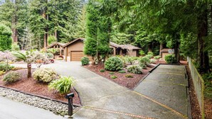 A residential area with two houses, a driveway, and a well-maintained garden with various plants and trees.