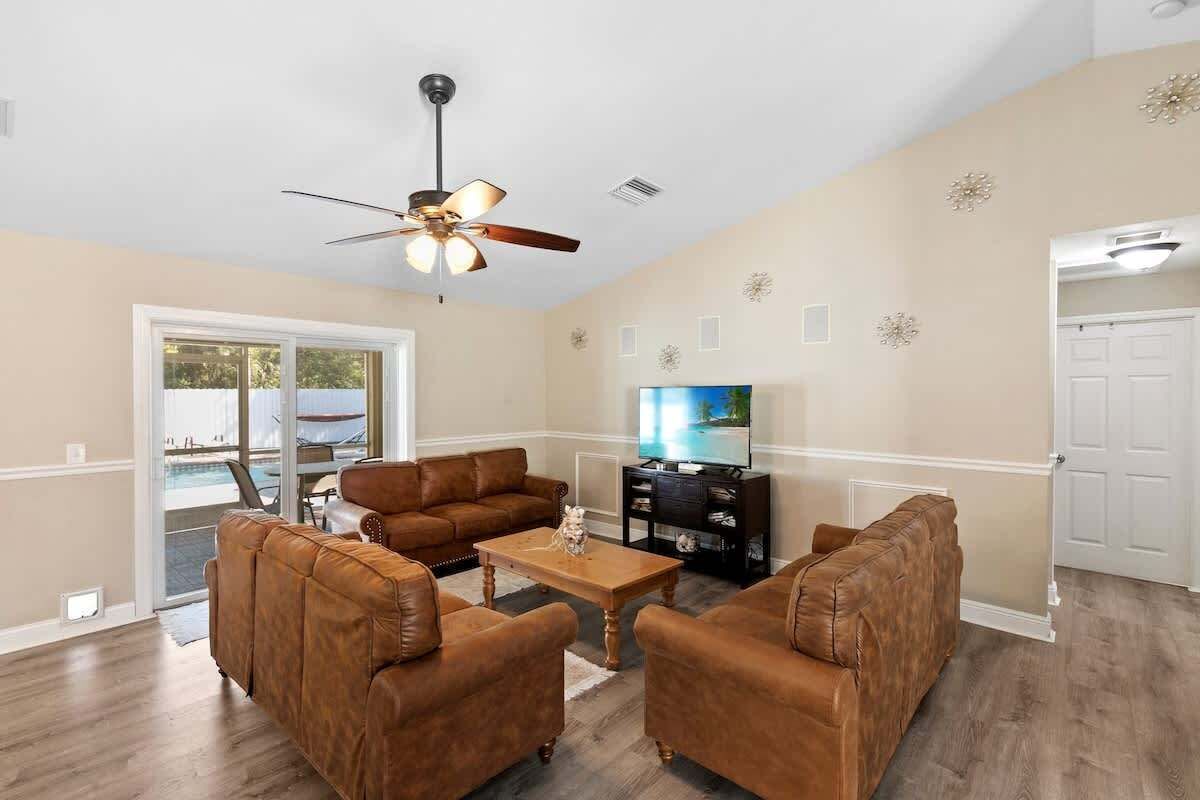 A living room with a brown leather sofa set, a wooden coffee table, a ceiling fan, and a television.