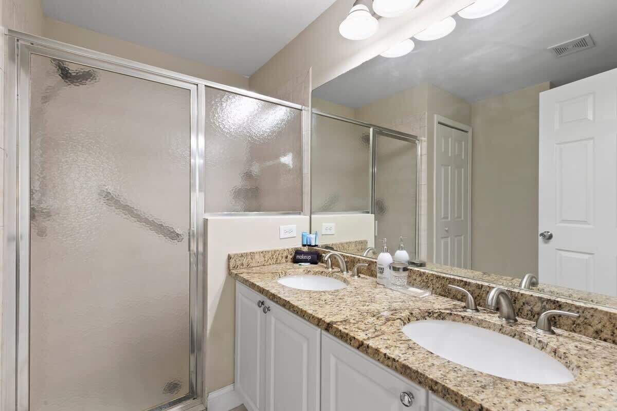 Une salle de bain dotée d’un meuble-lavabo à deux vasques, d’un grand miroir et d’une cabine de douche.