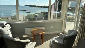 Une pièce dotée d’une grande fenêtre donnant sur la mer et la côte rocheuse. On y trouve deux chaises et une petite table.