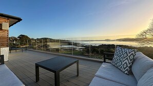 Une terrasse dotée d’un canapé et d’une table, offrant une vue panoramique sur un paysage pittoresque avec des collines et une étendue d’eau.