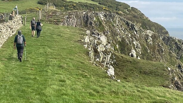 Une colline herbeuse avec une falaise rocheuse et une clôture en bois.