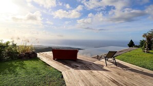 Terraza de madera con un sofá rojo y una silla, con vistas a una masa de agua y una tierra distante.