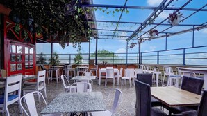 Un café en plein air avec des chaises et des tables en plastique blanc, une porte rouge et des plantes suspendues.