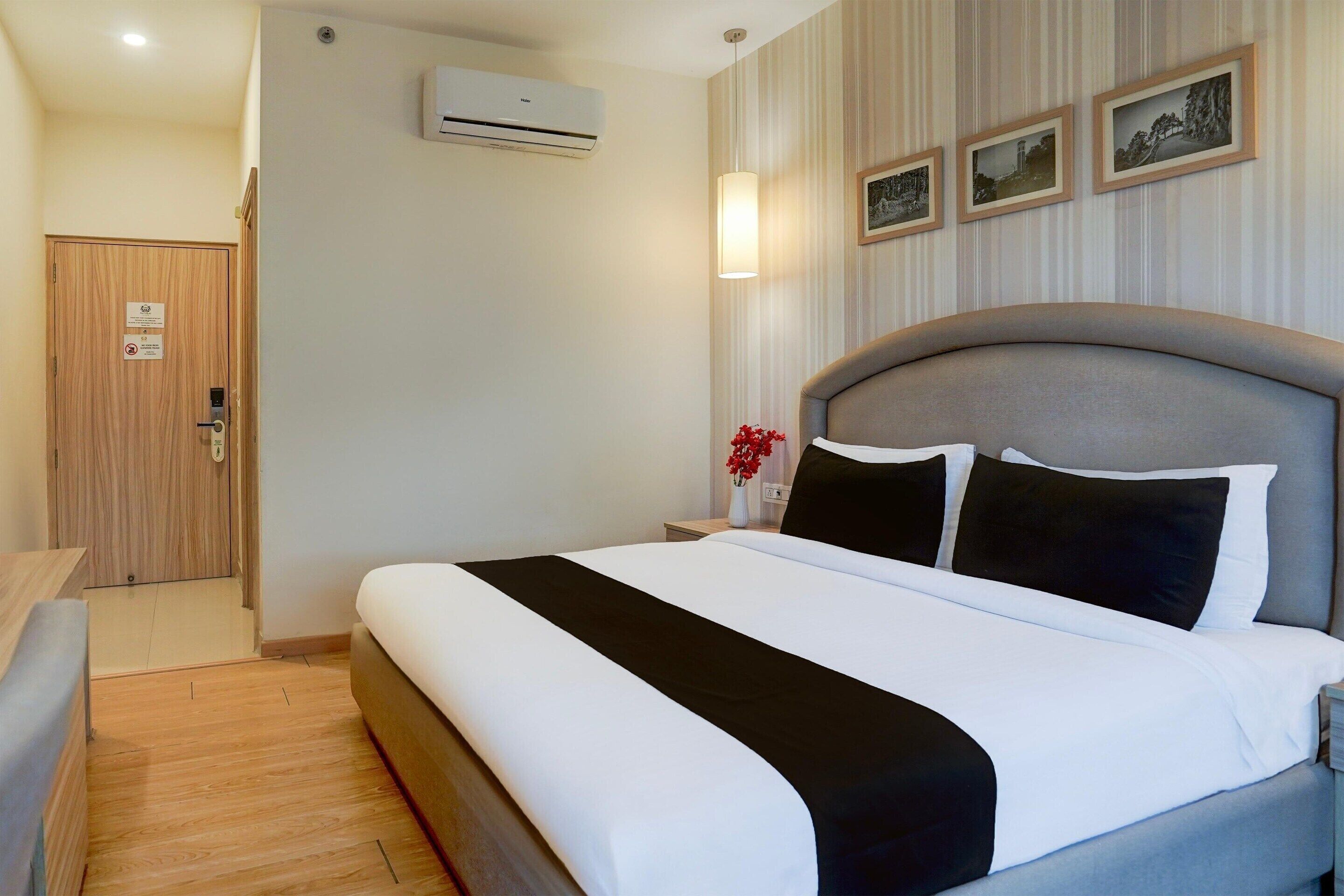 Habitación de hotel ordenada con una cama grande, una mesita de noche con un florero y un aire acondicionado de pared.