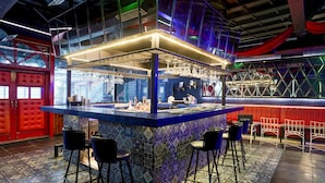 Un espace bar avec un comptoir recouvert de carreaux bleus, des tabourets de bar noirs et une porte rouge en arrière-plan.