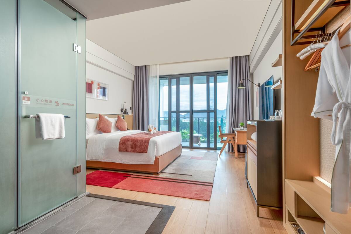 A modern hotel room with a large bed, a desk, and a view of the city.