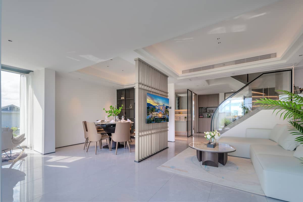 A modern living room with a dining area, a staircase, and a view of the outdoors.
