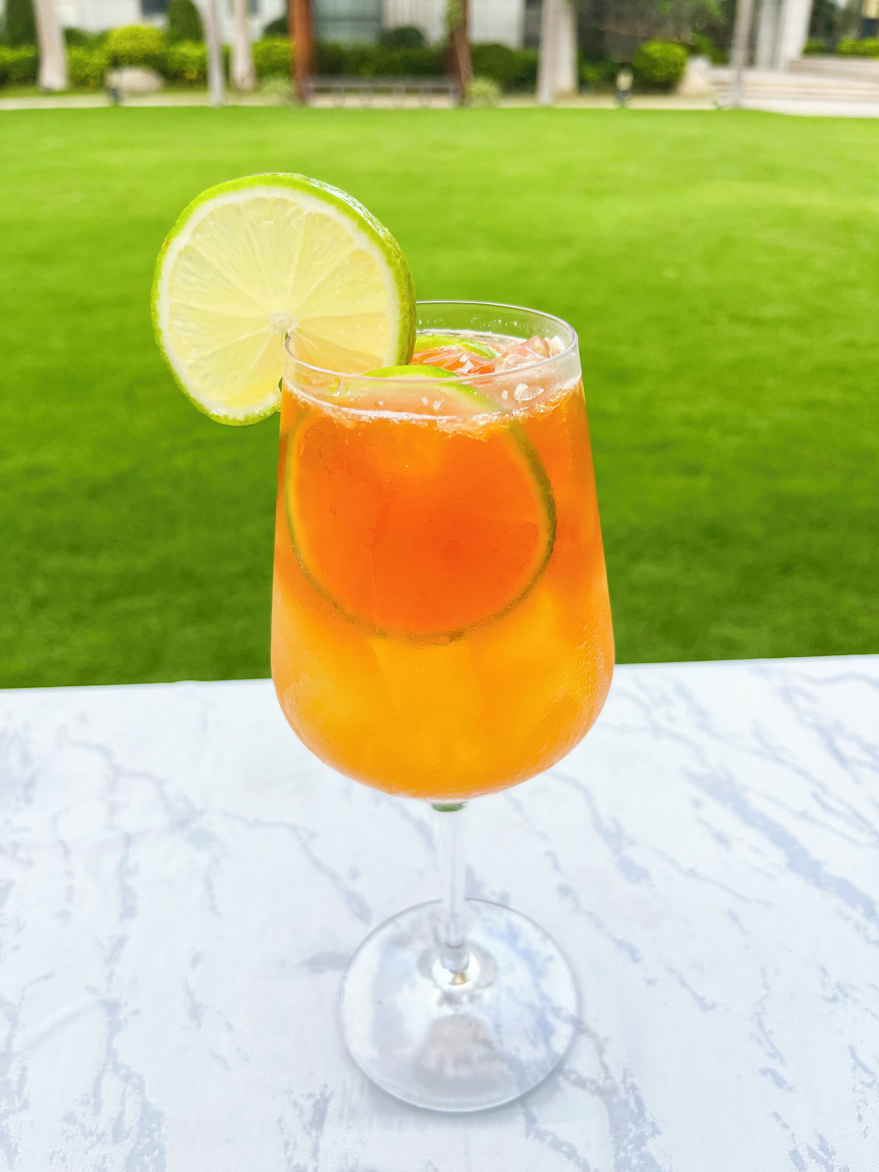 A glass of orange beverage with a lime slice on a marble surface.