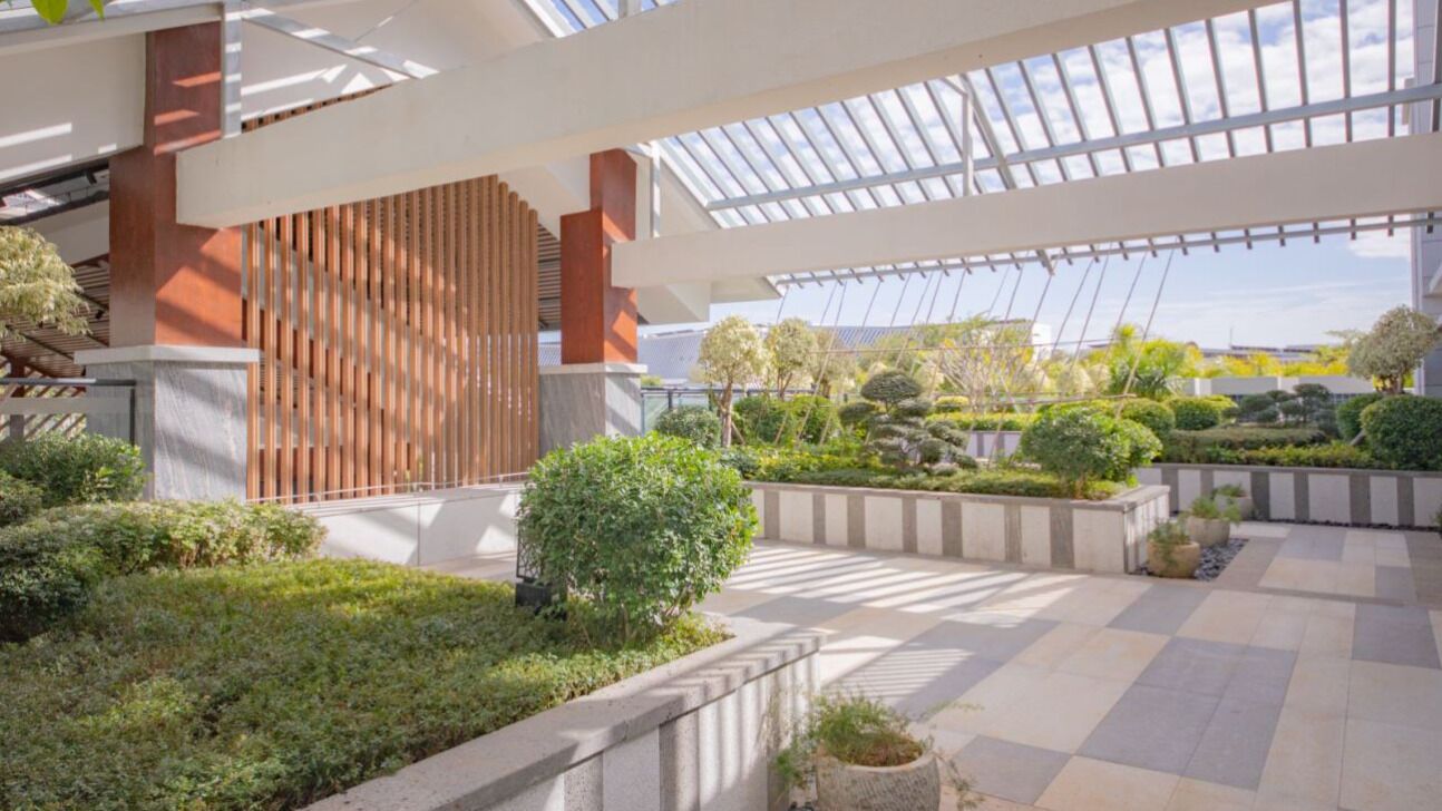 A spacious indoor garden with a glass ceiling, stone pathways, and neatly arranged greenery.