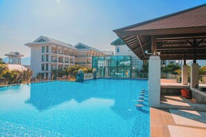 A swimming pool with a clear blue water surface, surrounded by a covered area with a roof and a glass wall. - Sanya Yalong Bay No.99 Resort Hotel (Sanya)