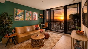 A living room with a sofa, round coffee table, and a view of the sunset through large windows.
