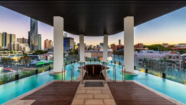 An infinity pool with a city view, surrounded by columns, and a covered area with seating.