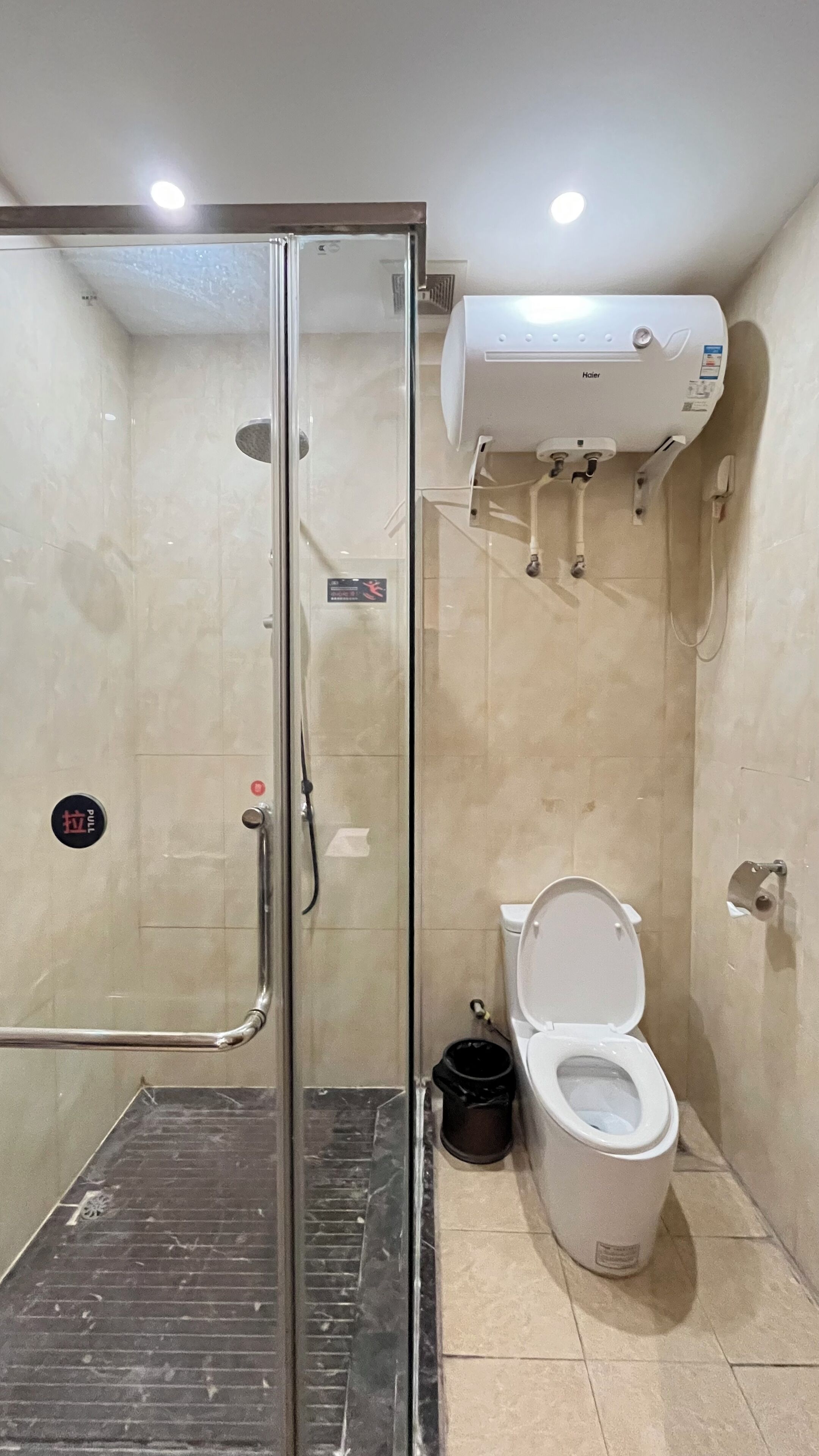 A bathroom with a glass shower enclosure, a toilet, and a white water heater mounted on the wall.