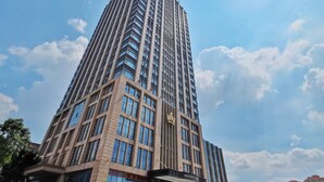 Ett högt, modernt hotell med en tydlig skylt som visar texten ”PRESIDENT HOTEL”. Fasadens utformning kombinerar glas och tegel, och byggnaden har flera våningar. I bakgrunden syns en klar himmel och moln.