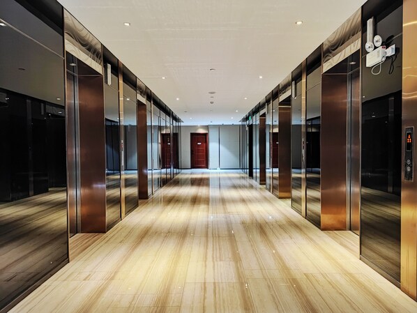 A modern hallway with elevators and glass doors, leading to a red door at the end.